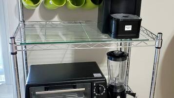 A kitchen cart with a coffee maker, a blender, and green mugs on the top shelf.