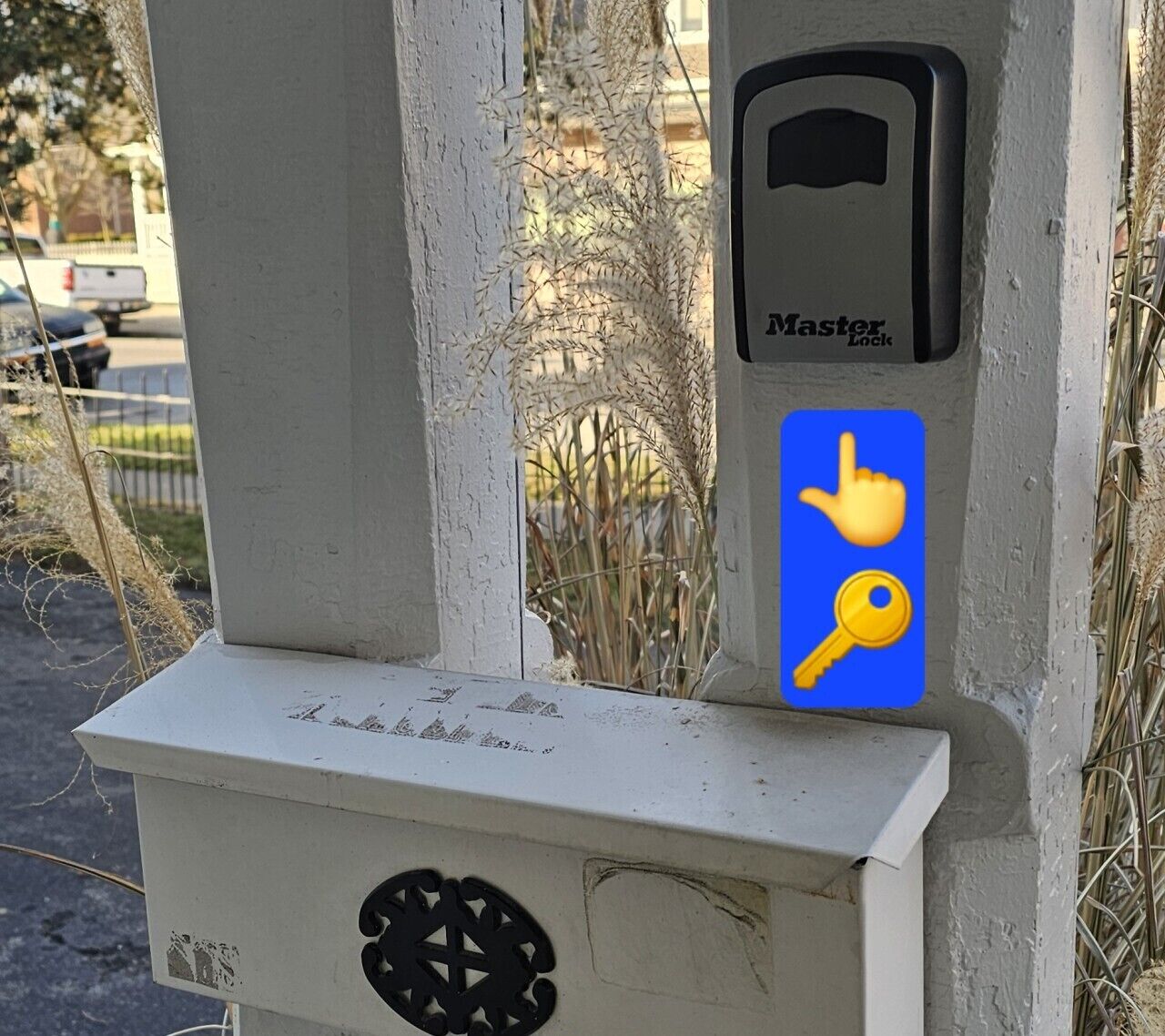 Un dispositif de verrouillage Master Lock fixé sur un poteau blanc, doté d’un clavier et d’un bouton bleu orné d’une icône représentant une main et une clé.