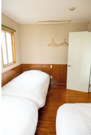 Two beds with white bedding are positioned in this simple room with a window on the left.
