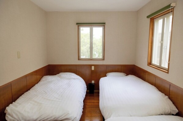 Two single beds with wooden headboards and white mattresses, a single window, and a neutral-colored wall.