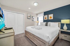 Ein ordentlich eingerichtetes Schlafzimmer mit einem Bett, Nachttischen, einer Lampe und einem Fernseher auf einem Schrank.