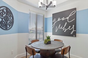 A dining area with a round table, four chairs, a decorative wall piece, and a window with blinds. - Near Westin | Top Floor | Hot Tub | Workspace (Scottsdale)