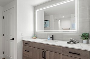 A modern bathroom with a large mirror, white tiles, a sink, and a potted plant. - Near Westin | Top Floor | Hot Tub | Workspace (Scottsdale)