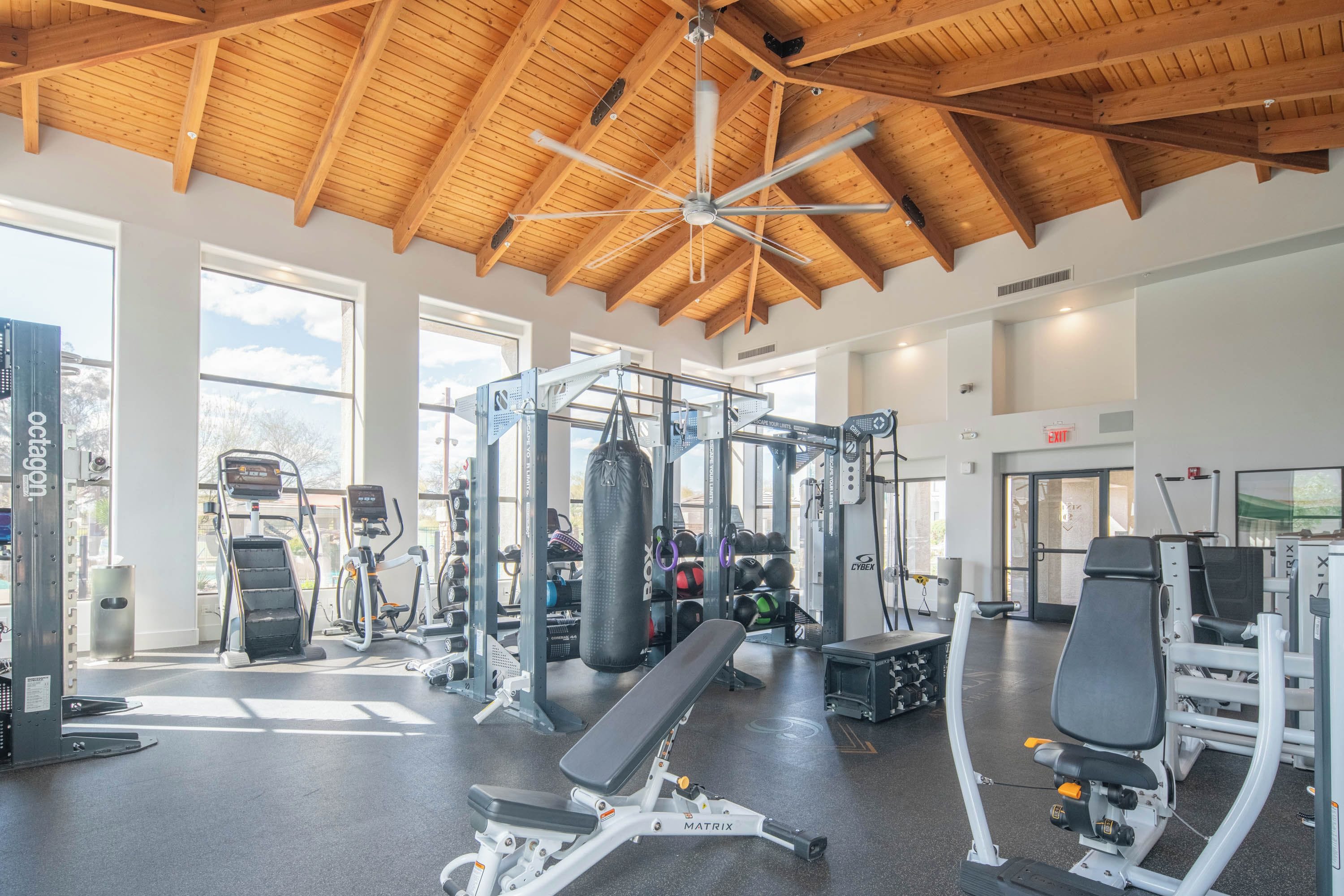 Ein Fitnessstudio mit unterschiedlichen Trainingsgeräten, großen Fenstern und einer Holzbalkendecke.