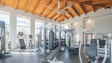 Ein Fitnessstudio mit unterschiedlichen Trainingsgeräten, großen Fenstern und einer Holzbalkendecke.