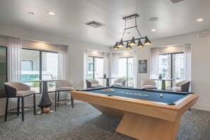 A pool table with chairs, a ceiling light fixture, and large windows with curtains.