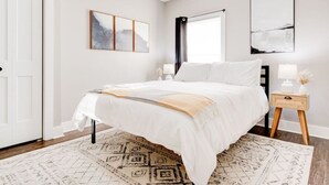 Un dormitorio con cama, mesita de noche, ventana y puerta.