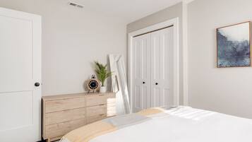 A bedroom with a bed, a dresser, a door, and a painting on the wall.