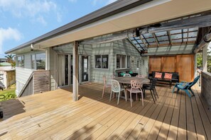A wooden deck with a dining table and chairs, a covered seating area, and a view of the house.