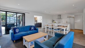 A modern living room with a blue sofa, a wooden coffee table, and a dining area with white chairs and a wooden table.
