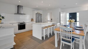 A modern kitchen with white cabinetry, a central island with bar stools, a built-in oven, and a stainless steel refrigerator.