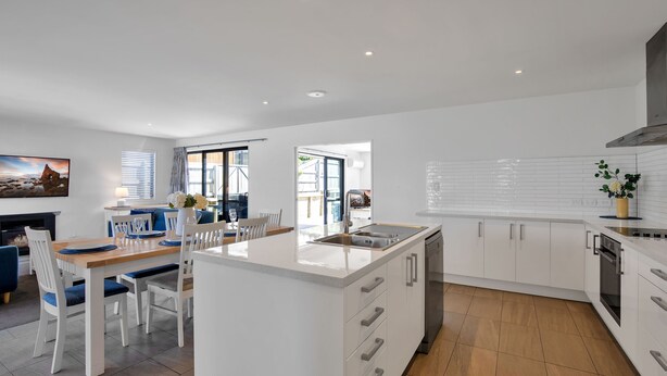 A modern kitchen with white cabinetry, a central island, and a dining area with white chairs and a wooden table.