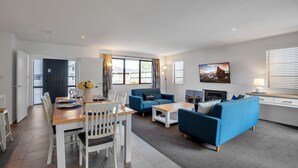 A modern living room with a dining area, blue sofas, a fireplace, and a large window with curtains.