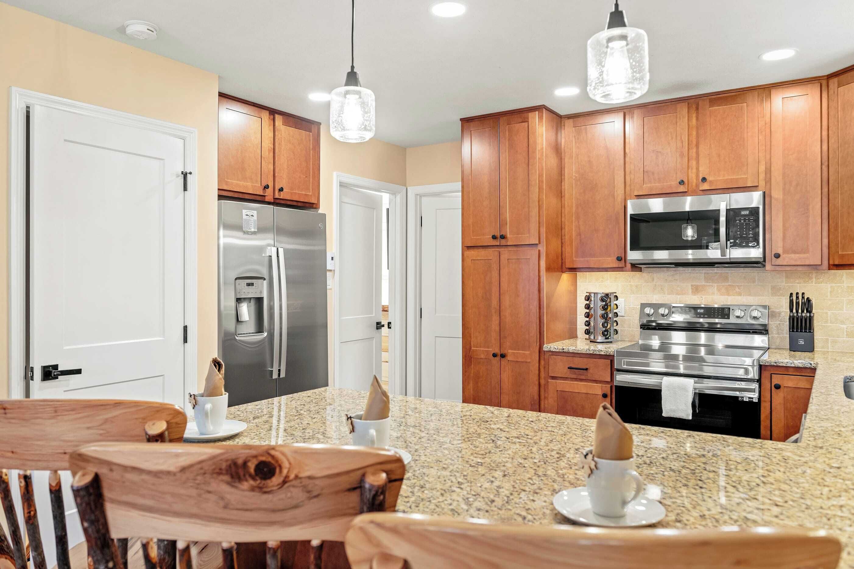 A modern kitchen with wooden cabinets, stainless steel appliances, granite countertops, and pendant lighting.