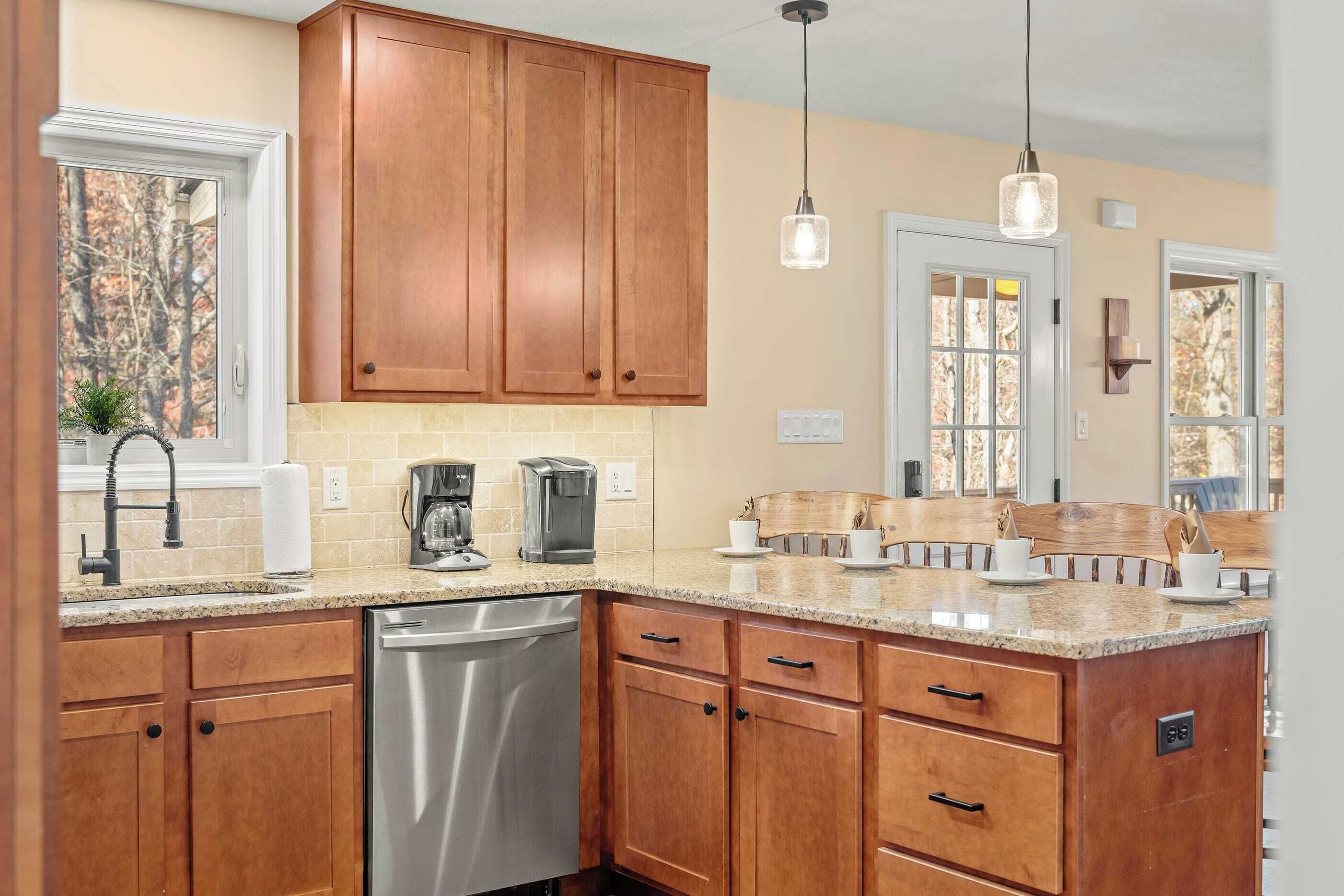 A kitchen with wooden cabinets, a stainless steel dishwasher, a granite countertop, and pendant lighting.