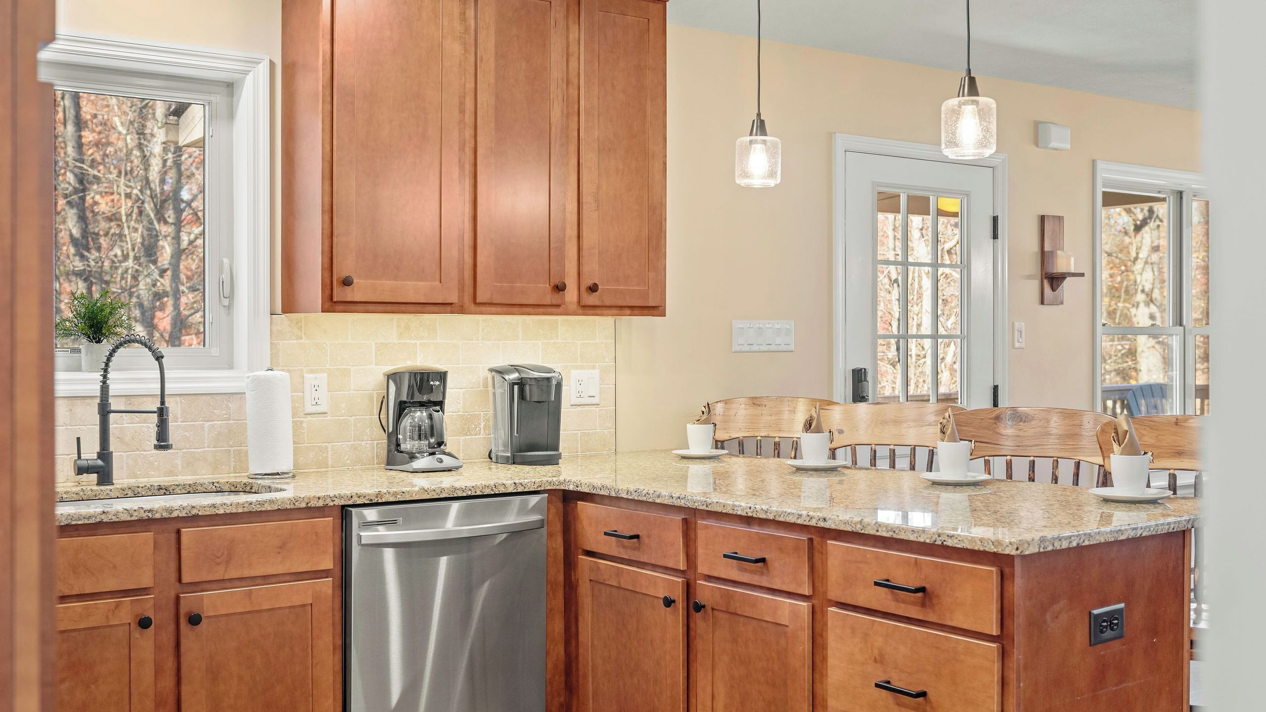 A kitchen with wooden cabinets, a stainless steel dishwasher, a coffee maker, and a dining area with a wooden table and chairs.