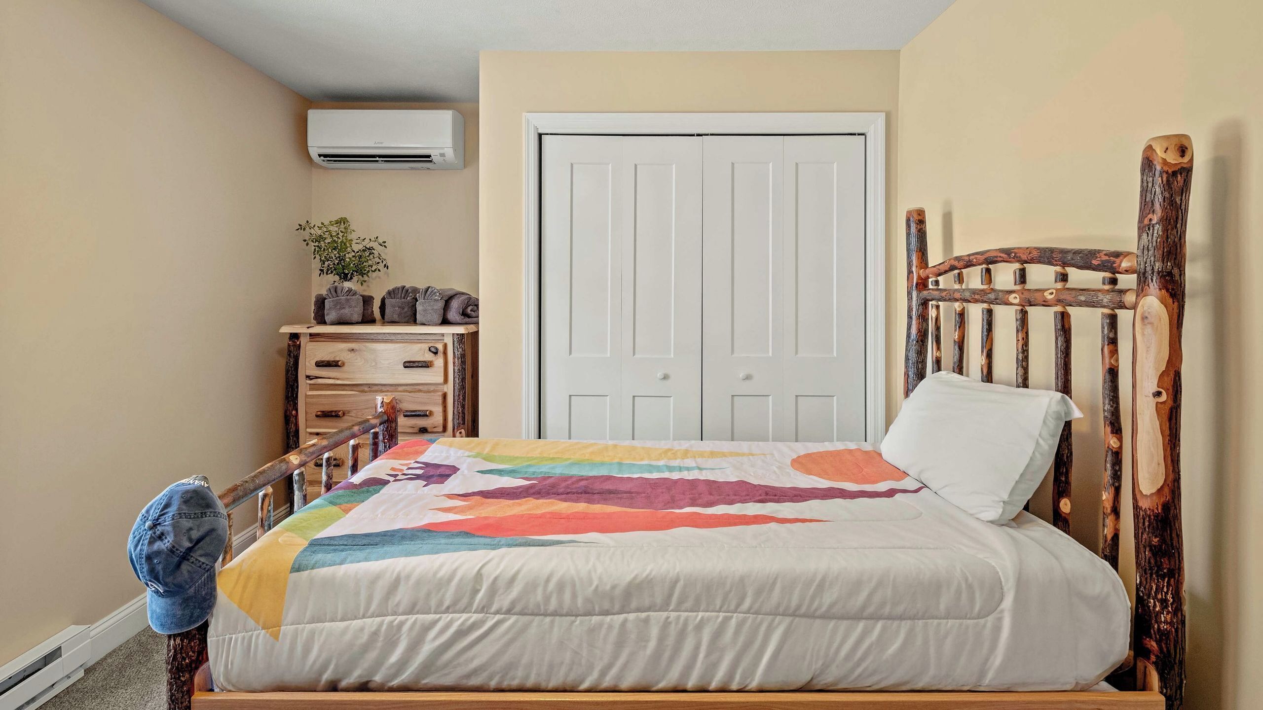 A bedroom with a bed, a wooden headboard, a dresser, a plant, and a white door.