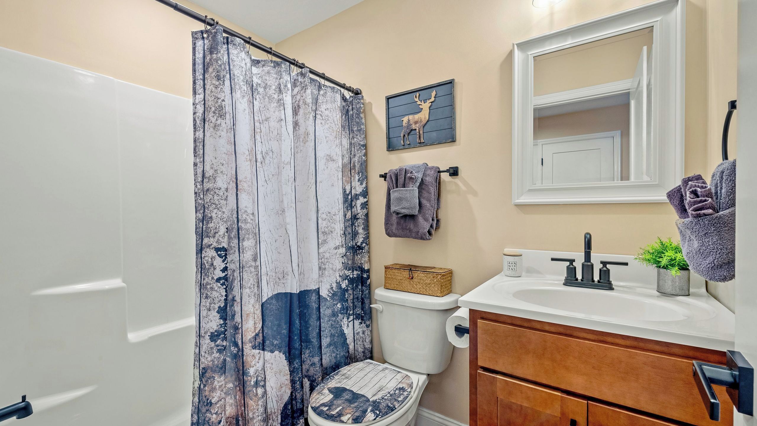 Un baño con cortina de ducha rústica, inodoro, lavabo con espejo y un armario de madera.