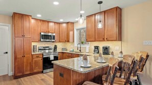 A kitchen with wooden cabinets, a granite countertop, and a bar area with rustic chairs. - Stephen Way by Avantstay Hot Tub + Game Room Albrightsville (Albrightsville)