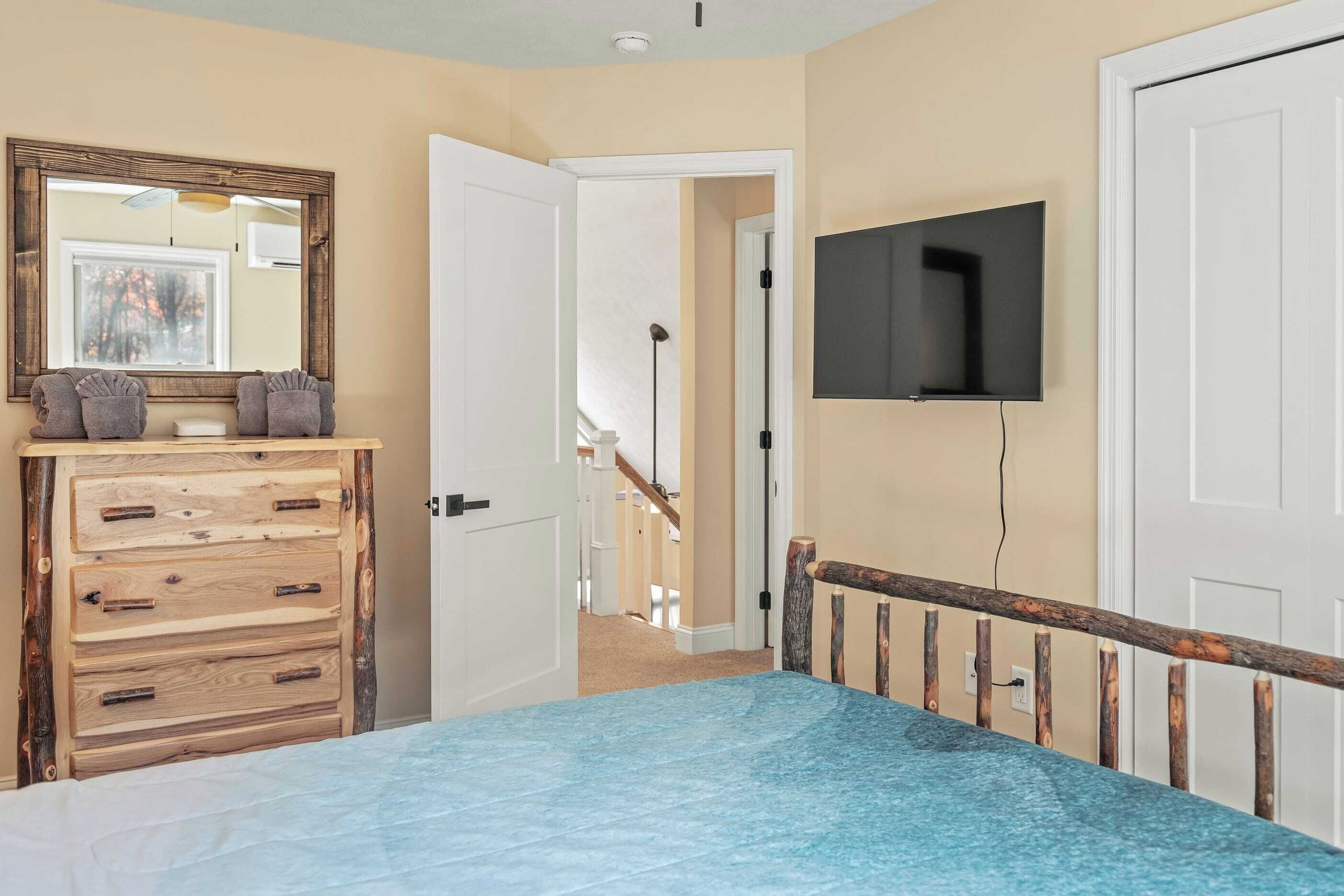 A bedroom with a bed, wooden dresser, TV, and a view of a staircase.