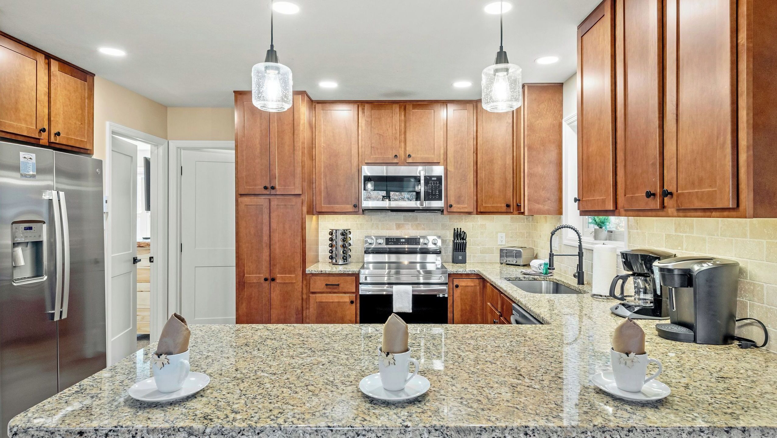 A modern kitchen with wooden cabinets, stainless steel appliances, granite countertops, and pendant lighting.