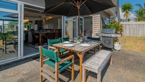 Um pátio externo com mesa e cadeiras de madeira, e um grande guarda-sol.