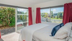 Quarto com cama grande, cortinas vermelhas e vista para um jardim e rua.