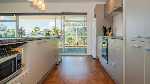 Cozinha moderna com janela grande, piso de madeira e eletrodomésticos de aço inoxidável.