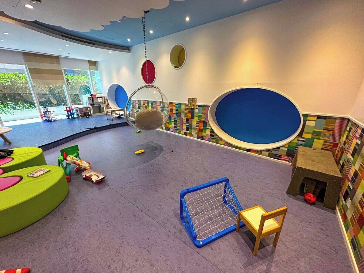 Ein Spielbereich für Kinder mit bunten Sitzgelegenheiten, einem blauen Gitterbett und Hängeschaukeln.