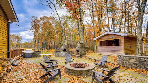 A stone fire pit surrounded by Adirondack chairs, a stone oven, and a wooden cabin in a wooded area. - Private Hot Tub on 10 Acres: Cozy Catskill Getaway (Catskill)