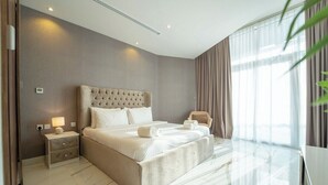 Habitación de hotel moderna con una cama grande, una mesita de noche con lámpara y vistas al exterior a través de cortinas traslúcidas.
