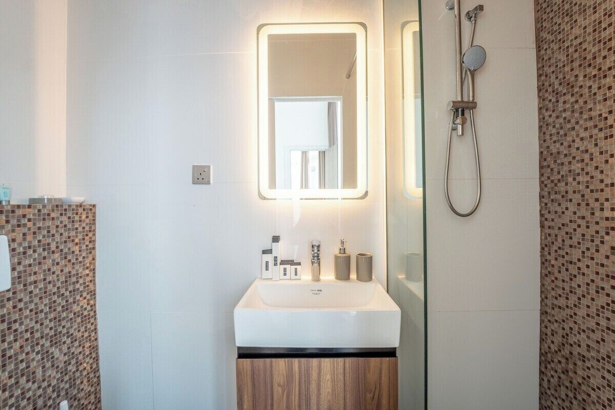 A modern bathroom with a large mirror, a shower, and a sink with toiletries.