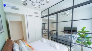 Ett modernt hotellrum med en stor säng, en glasvägg och utsikt över vardagsrummet.