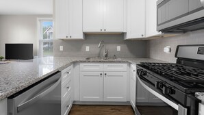 A modern kitchen with white cabinets, a granite countertop, a stainless steel stove, and a built-in dishwasher. - Downtown Columbus~Stunning Upscale 1 bd Suite (Columbus)