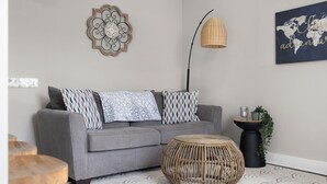 A modern living room with a grey sofa, patterned cushions, a woven side table, a round wicker coffee table, a floor lamp, and a world map artwork on the wall. - Downtown Columbus~Stunning Upscale 1 bd Suite (Columbus)