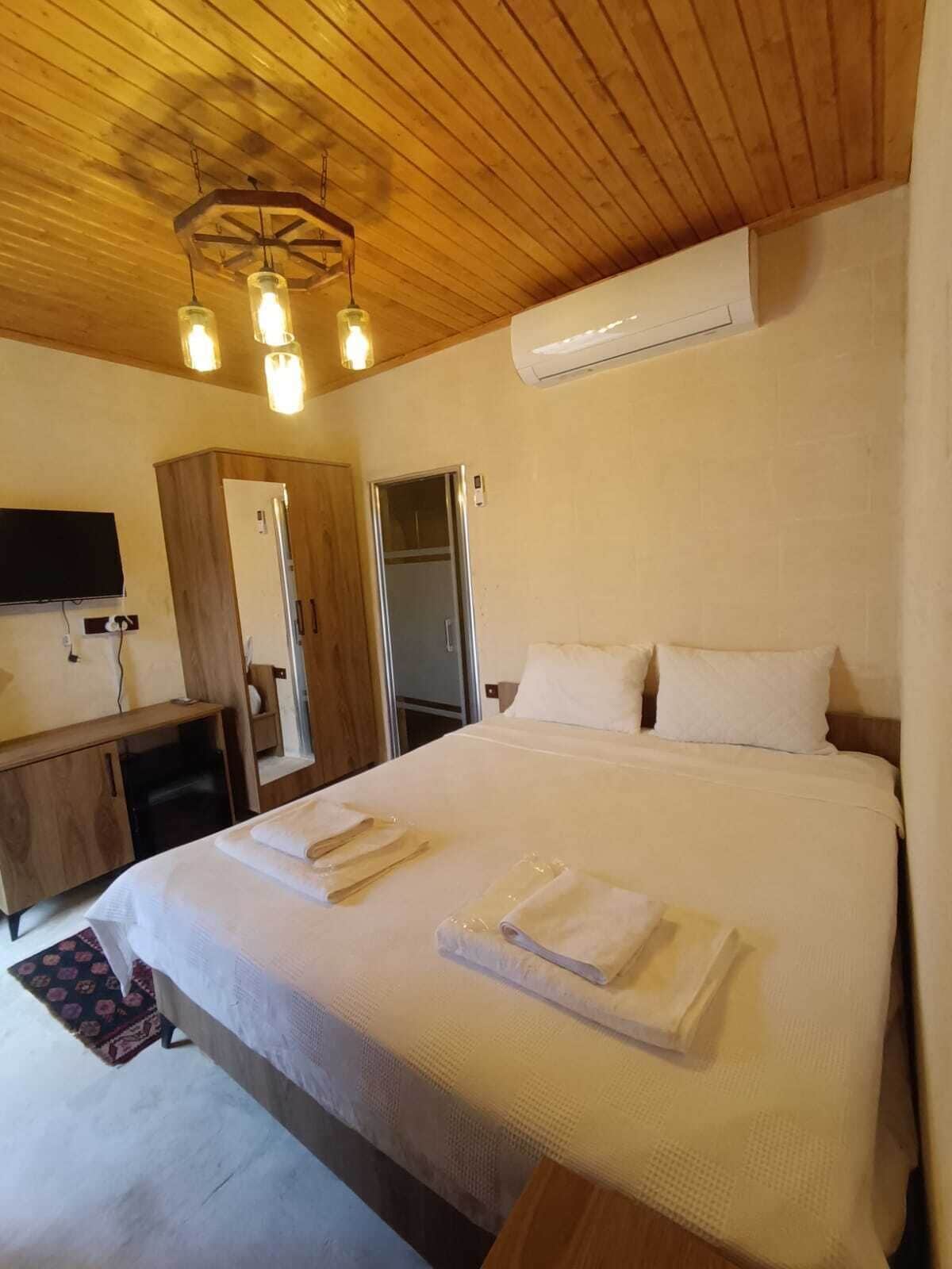 Habitación de hotel con techo de madera, cama con ropa blanca, televisor de pantalla plana, armario y aire acondicionado.