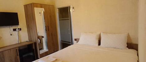 Habitación de hotel con techo de madera, cama con ropa blanca, televisor de pantalla plana, armario y aire acondicionado.