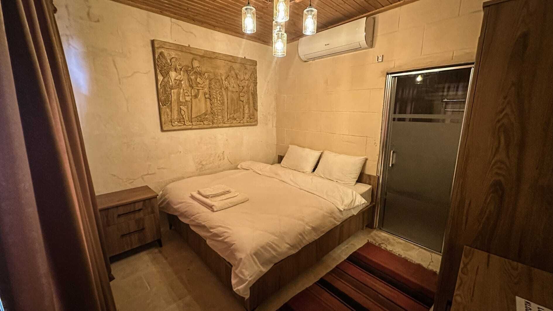Un dormitori amb un llit, una tauleta de nit, una obra d'art penjada a la paret, una dutxa i un sòl de fusta.