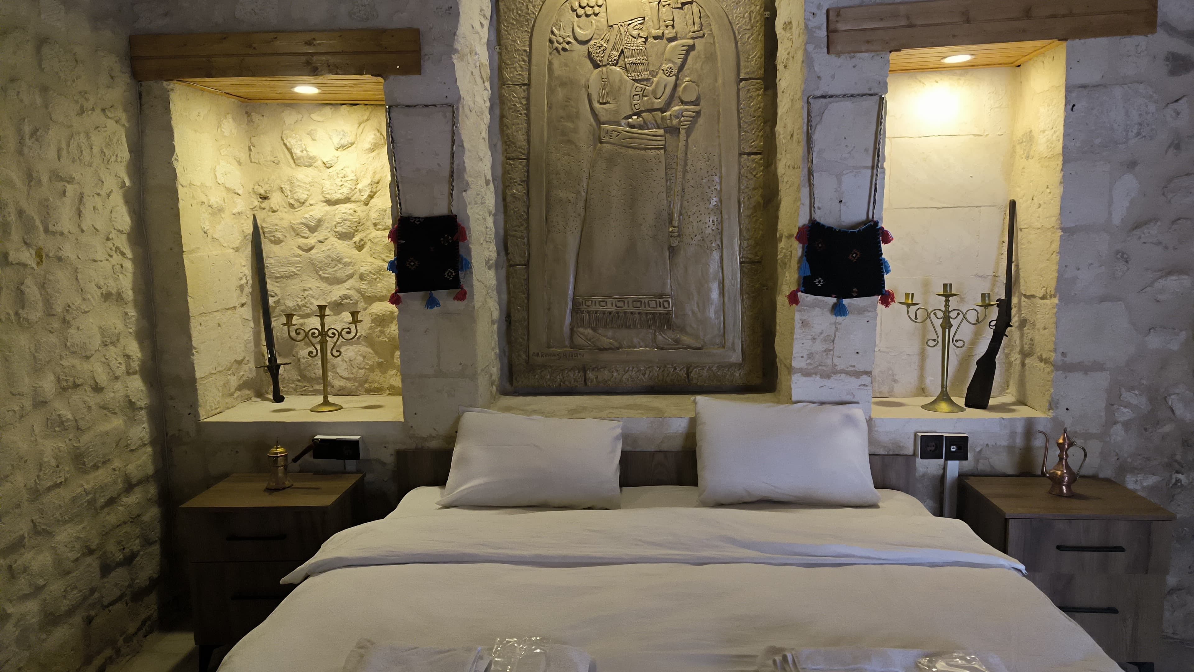 Ein Schlafzimmer mit einem großen Bett, zwei Nachttischen, einer Steinwand und einer geschnitzten Holzvertäfelung über dem Bett.