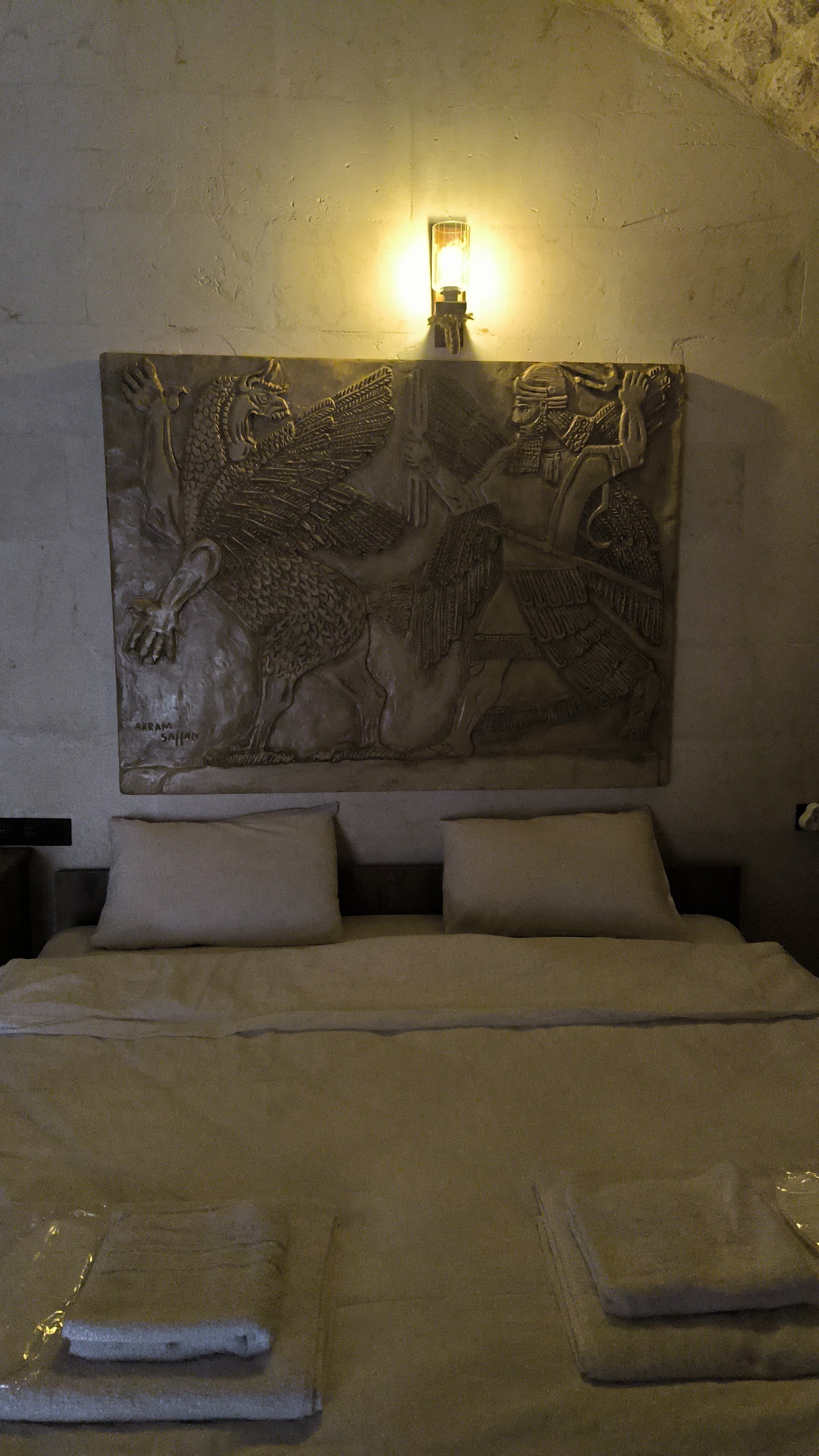 Ein Bett mit großem Wandbild, das eine historische Szene zeigt, einer Nachttischlampe und einem Kopfteil.