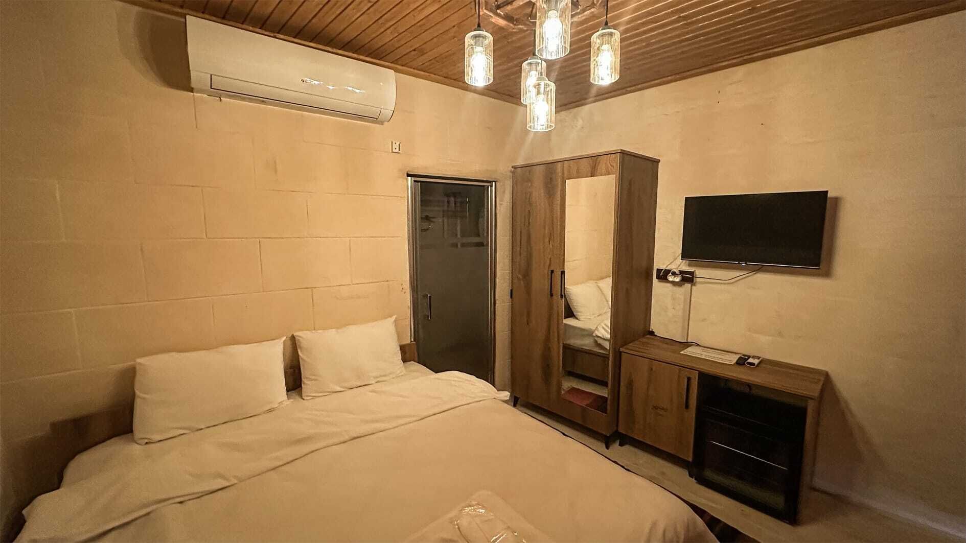 A bedroom with a bed, a wardrobe, a television, and an air conditioning unit.
