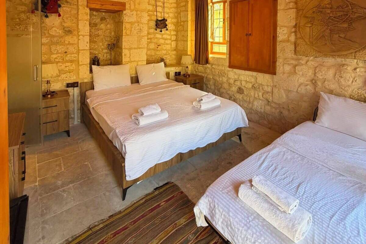 A stone-walled bedroom with two beds, wooden ceiling, and a hanging light fixture.