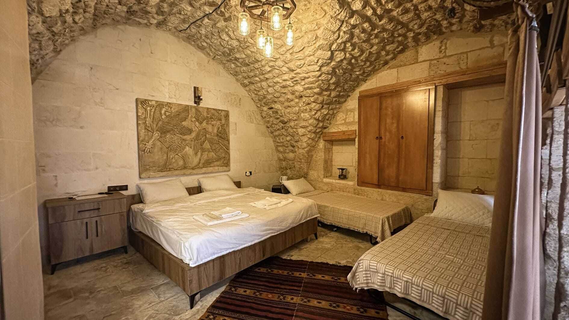 A bedroom with two beds, a stone ceiling, and a wooden wardrobe.