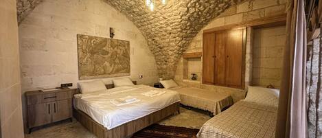 A bedroom with two beds, a stone ceiling, and a wooden wardrobe.