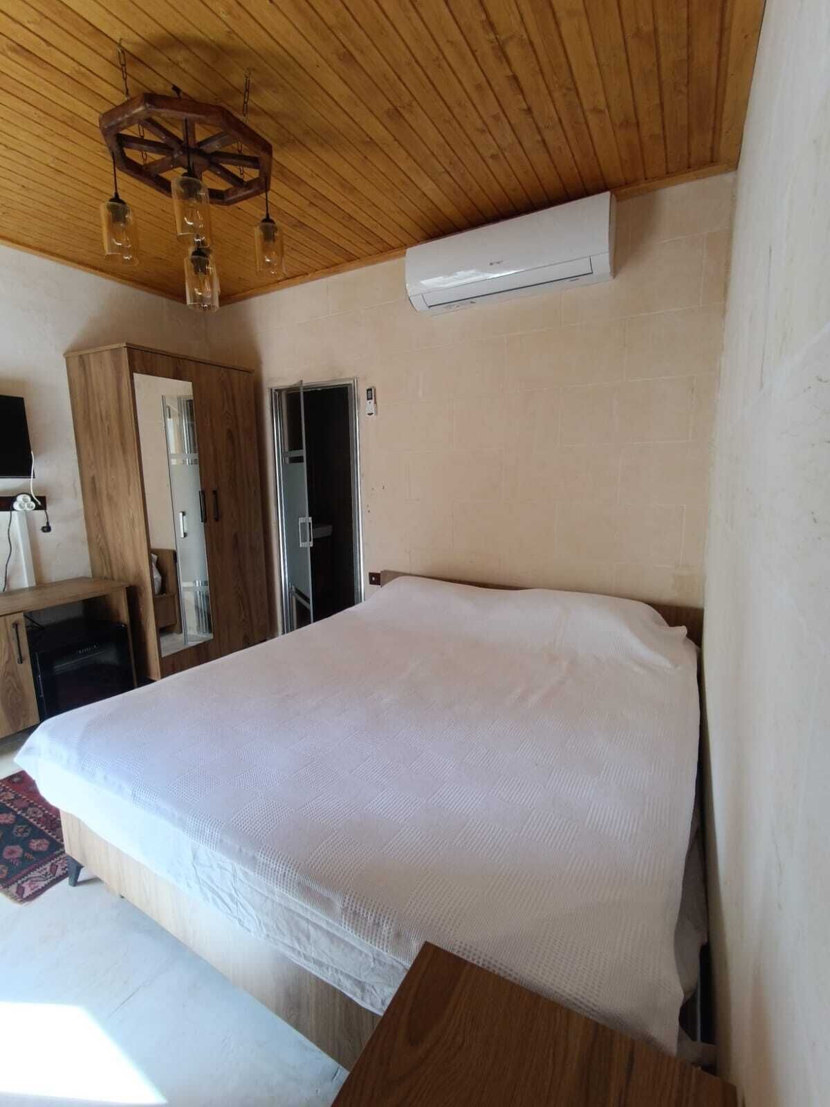 A bedroom with a wooden ceiling, a bed, a wardrobe, and an air conditioning unit.