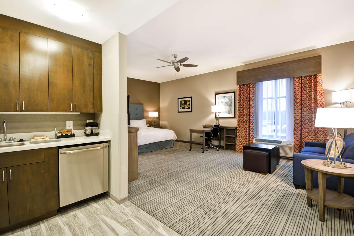 Habitación de hotel con kitchenette, cama, escritorio, silla, sofá y ventilador de techo.