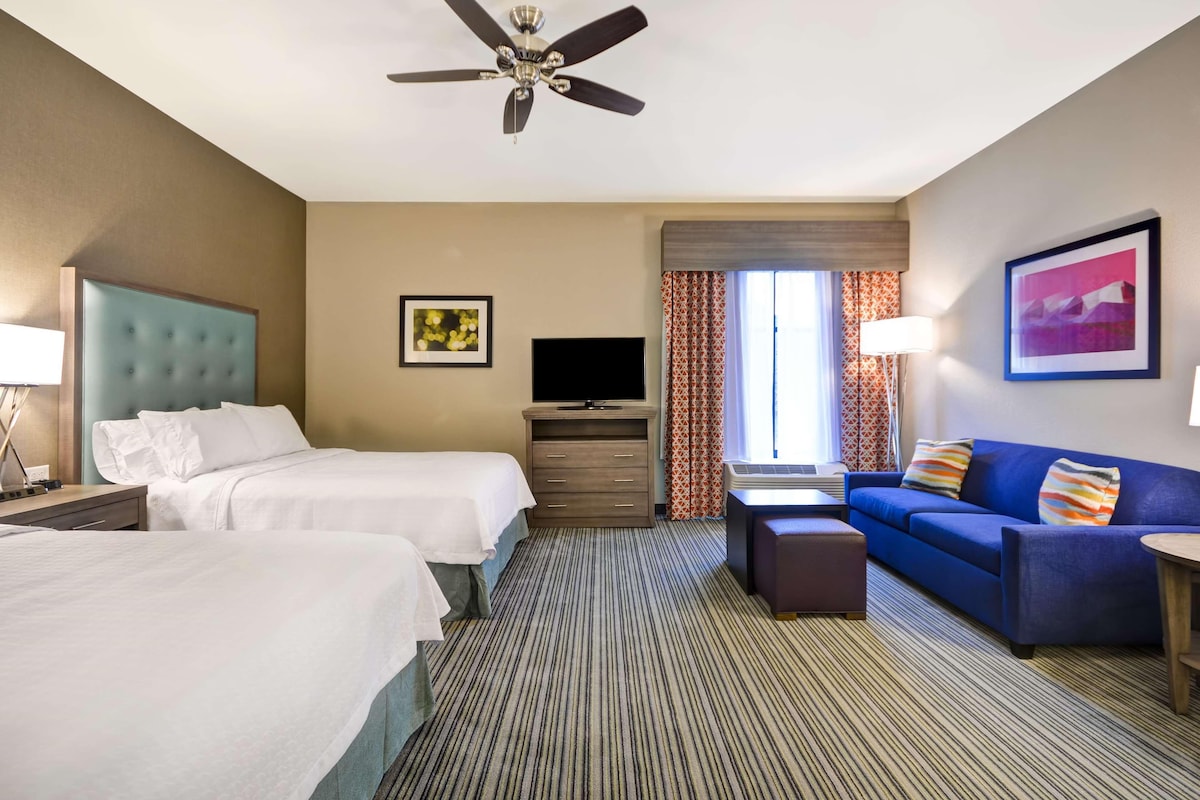 Una habitación de hotel con dos camas, un sofá azul, un televisor y un ventilador de techo.