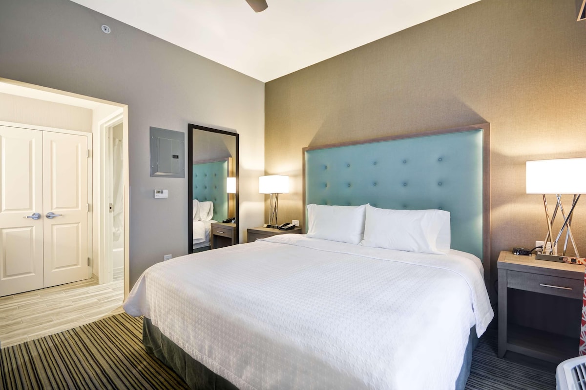 Habitación de hotel con una cama grande, una mesita de noche con lámpara, un espejo y un armario.
