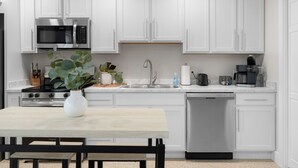 Una cocina moderna con alacenas blancas, un microondas de acero inoxidable, una estufa a gas, un fregadero y un lavavajillas.