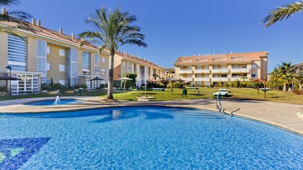 A swimming pool surrounded by buildings with balconies, palm trees, and a clear sky. - Charming 2-bedroom apartment with WiFi, AC in fantastic Platja de l'Arenal (Platja de l'Arenal)